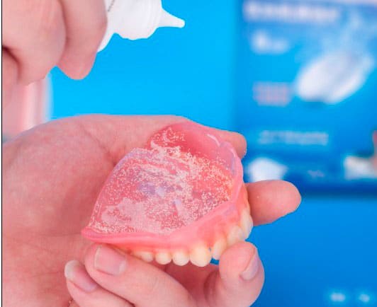 Aplicación de polvo adhesivo en dentadura postiza